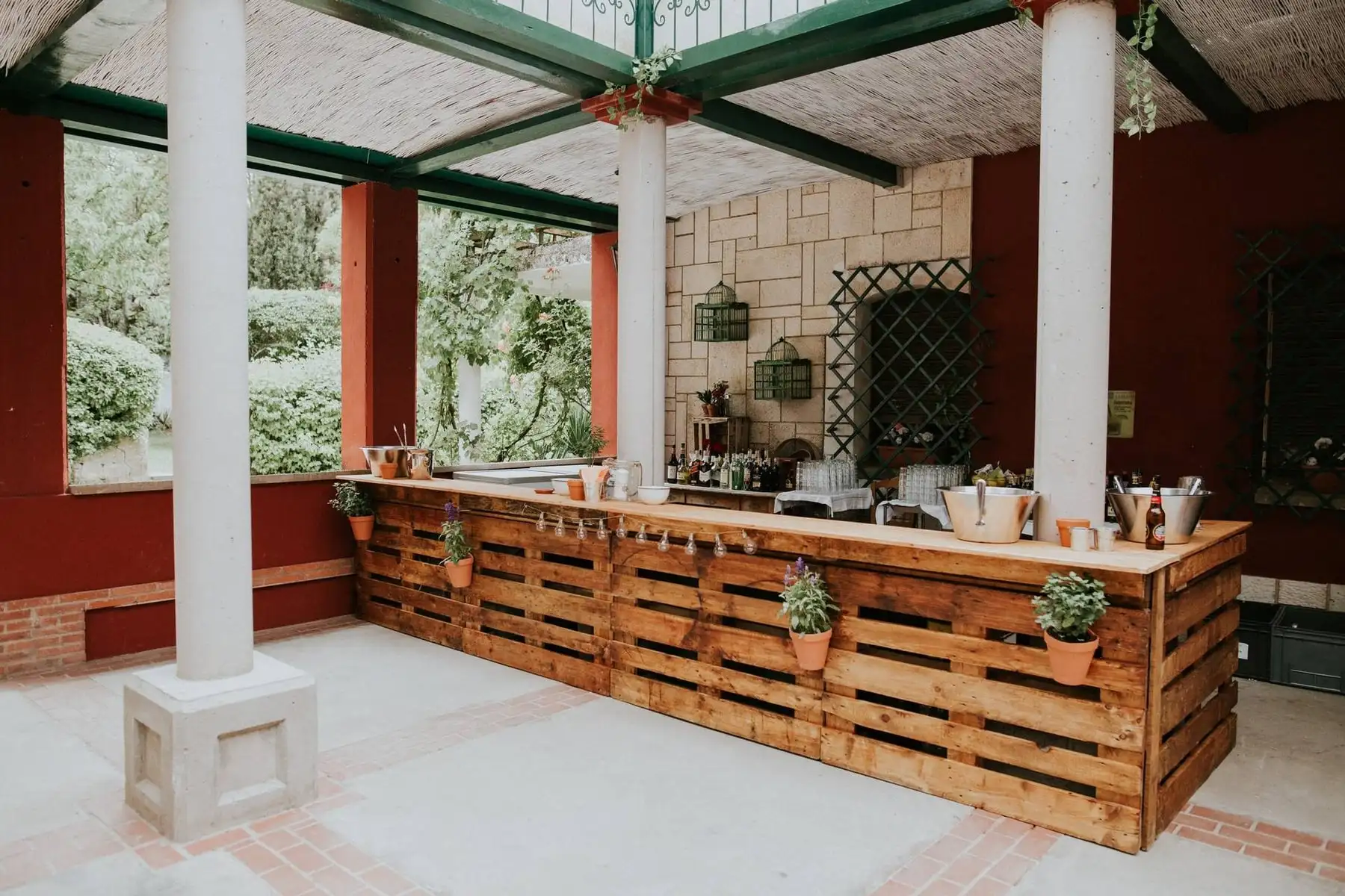 La barra de madera de palés bajo la pérgola del patio cubierto, con botellas y vasos a punto