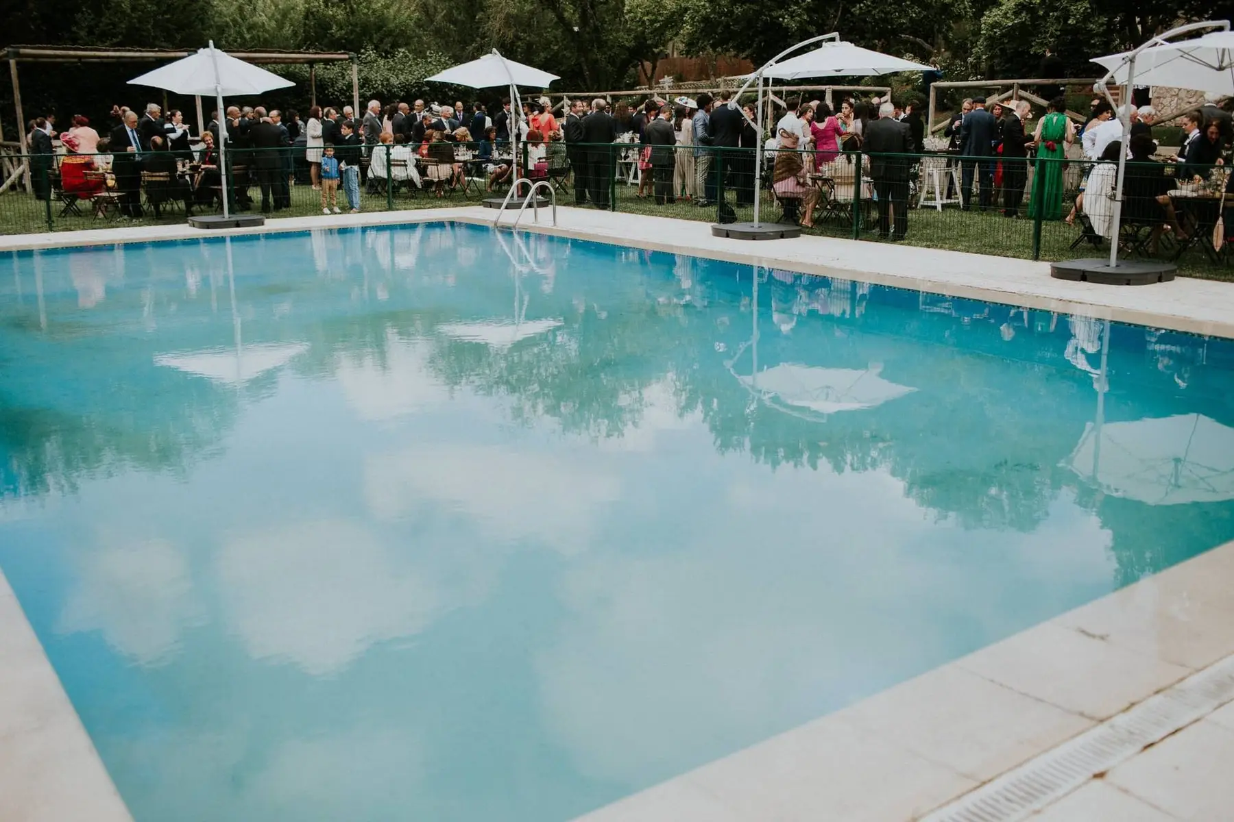 El cóctel de una boda junto a la piscina, con sombrillas blancas y los invitados al fondo