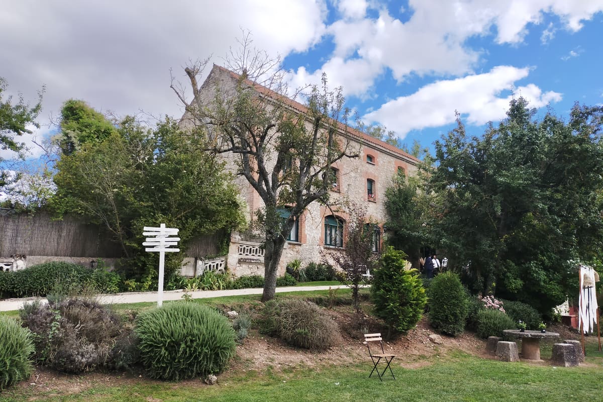 La casa de la Finca Puertas Verdes entre los árboles, con su fachada de piedra y ladrillo y el césped en primer plano